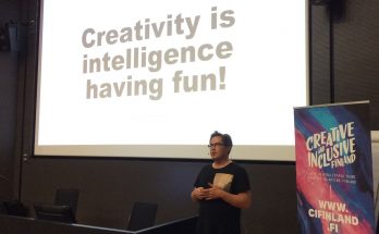 Panu Mäenpää puhumassa. Taustalla näkyy screen, jossa lukee "Creativity is intelligence having fun!"